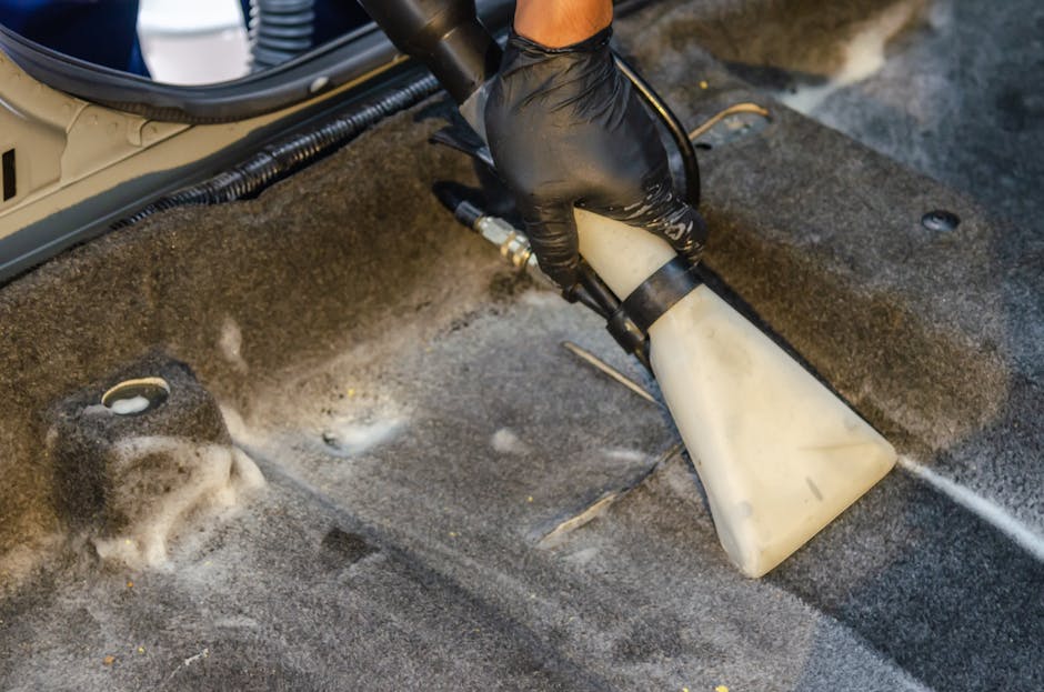 commercial carpet cleaning A hand in a glove using a vacuum to clean a car interior carpet, removing dirt effectively.