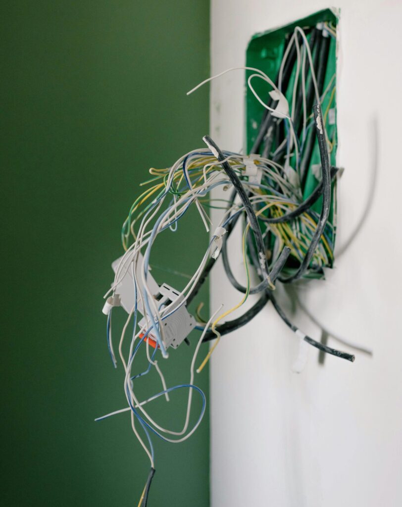 Opened power socket with various wires on white wall during repair at home