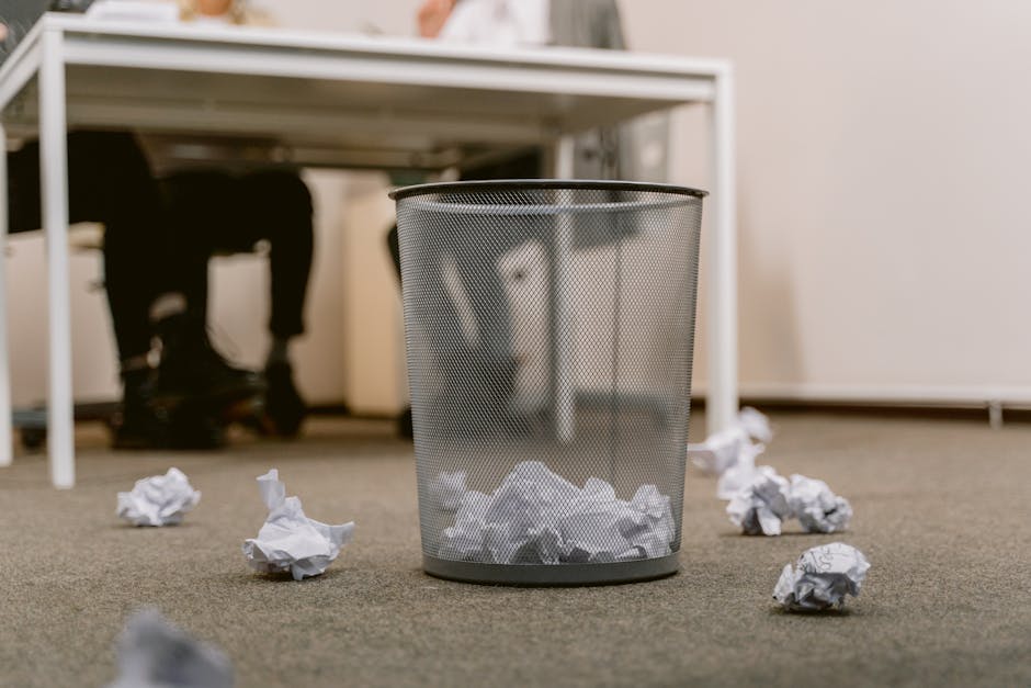 pexels-photo-6913195-6913195 Office floor with a visible trash bin and crumpled papers scattered around, blurring human figures.